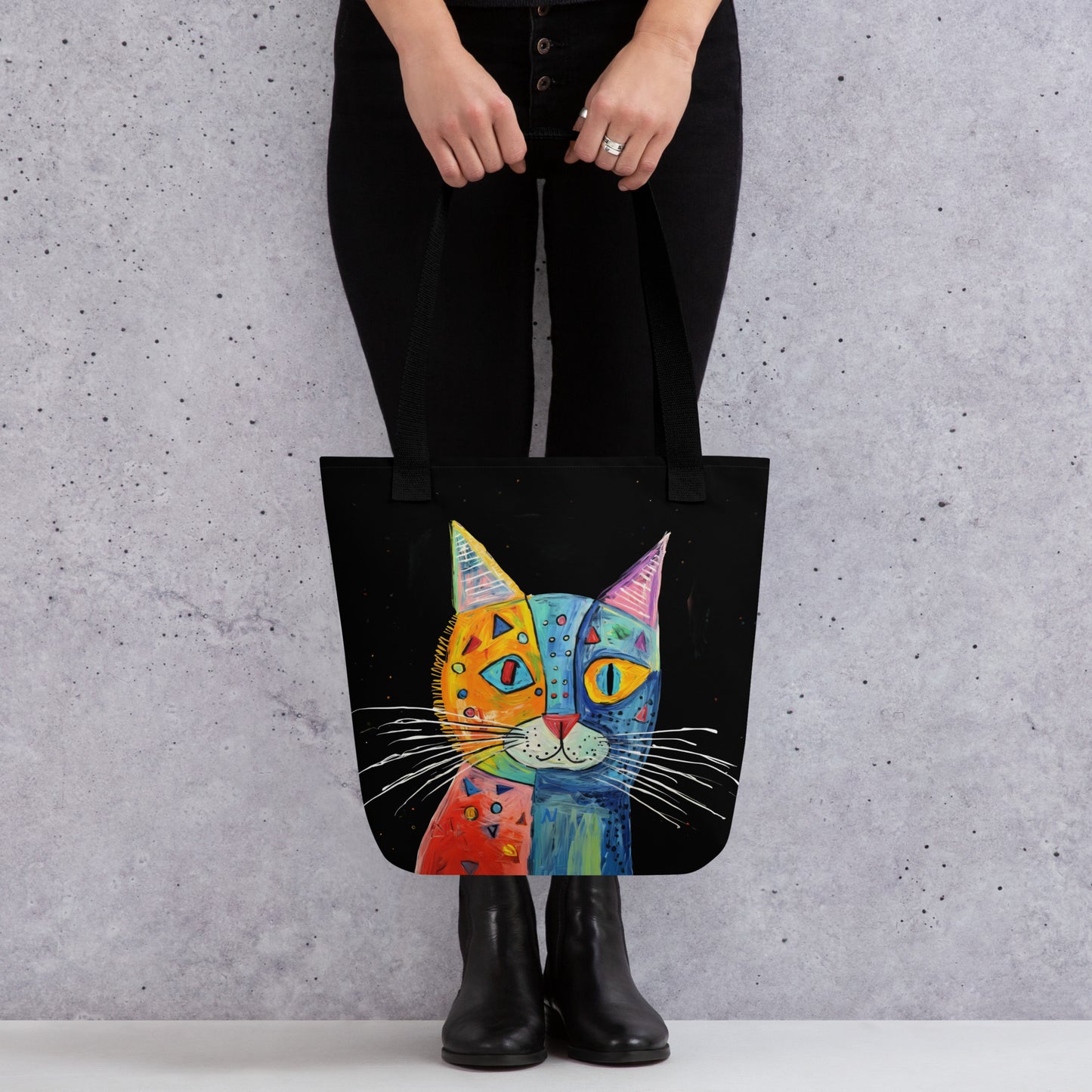 Tote bag with a colorful cat design held by a person against a gray background